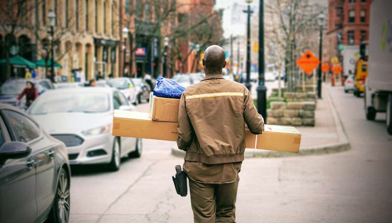 Một người giao hàng mang hai gói lớn màu nâu xuống một con phố trong thành phố