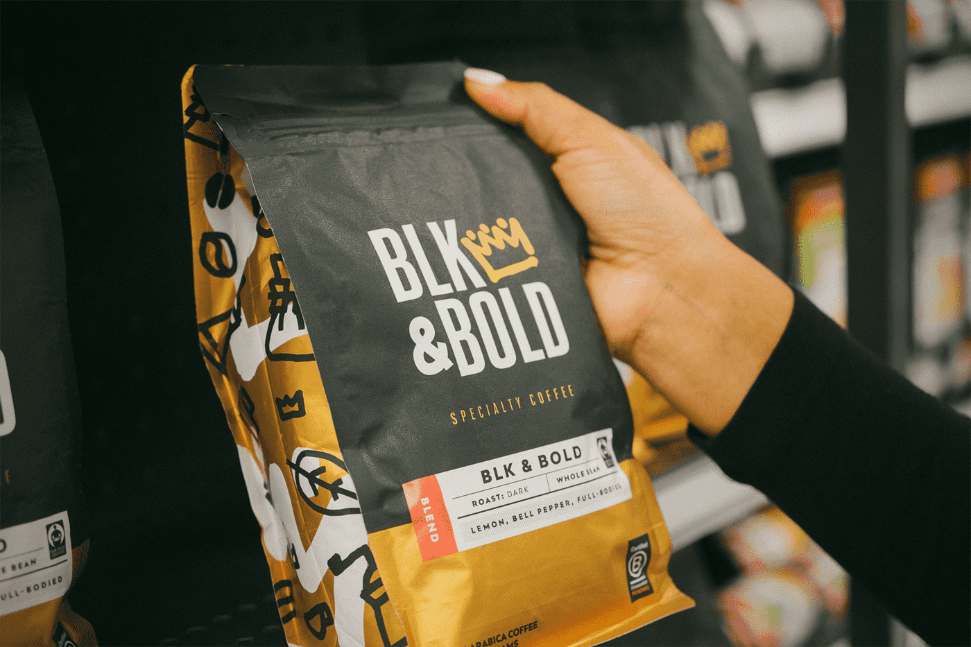 Một gói cà phê BLK & Bold được cầm bằng tay dựa vào một số kệ bán lẻ.