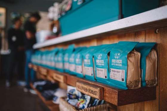 Một kệ gỗ được xếp với một số túi màu xanh có chứa hạt cà phê