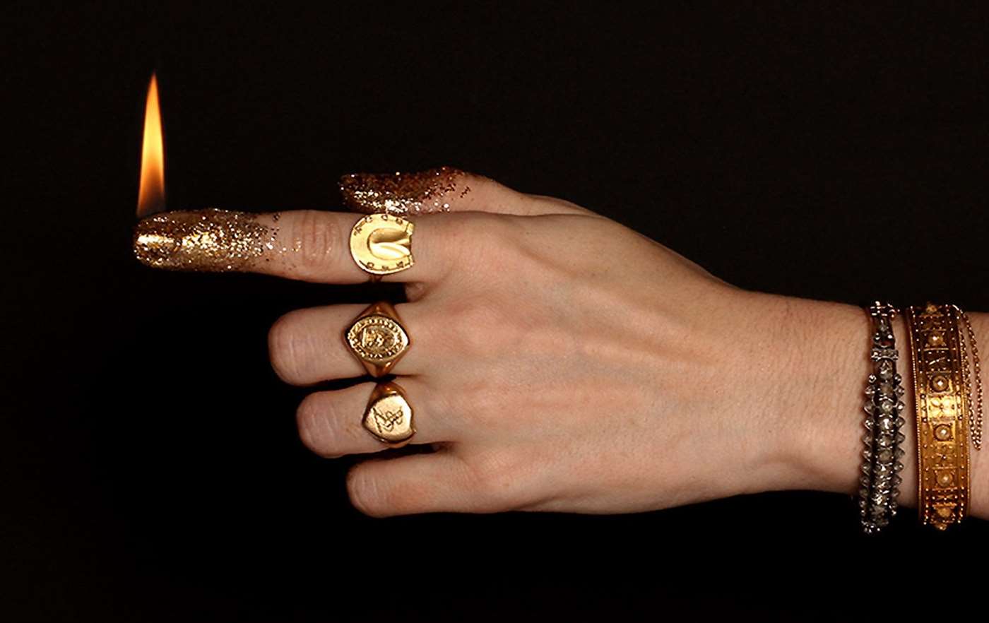 Tay đeo một vài chiếc nhẫn Erica Weiner cổ điển.  Ngón trỏ được dát vàng lấp lánh và được thắp sáng như một ngọn nến.