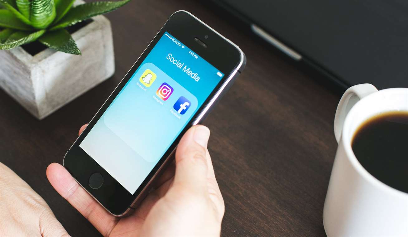 Một người cầm điện thoại di động hiển thị các biểu tượng Snapchat, Instagram và Facebook
