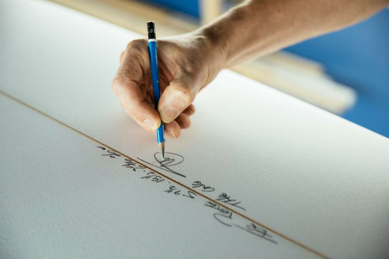 Cận cảnh bàn tay của Stef Aftanas ký tên lên ván lướt sóng bằng bút chì.