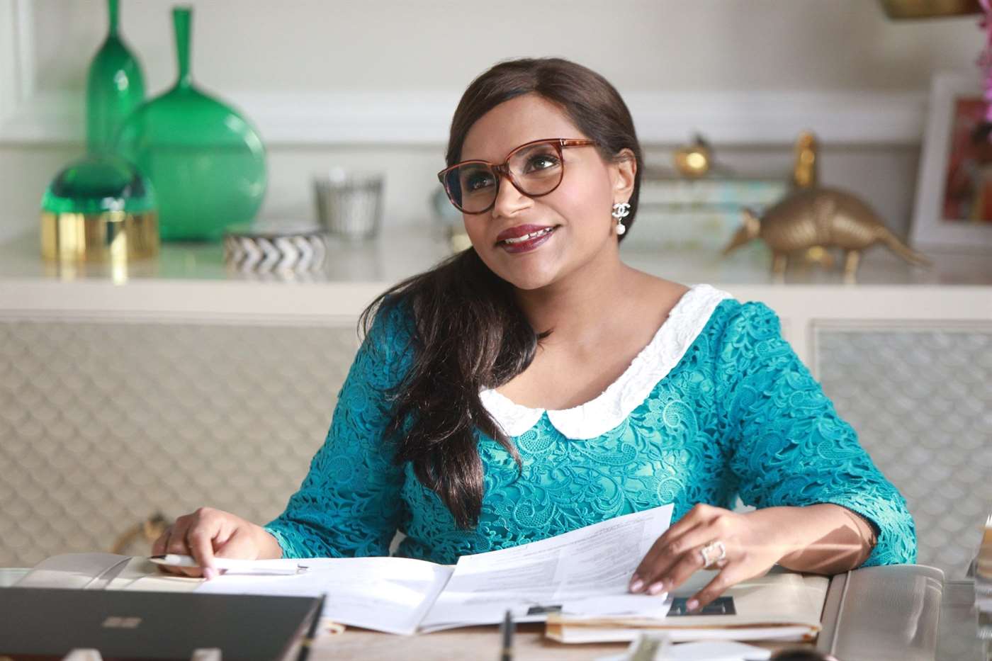 Nhân vật Mindi Lahiri ngồi sau bàn làm việc trong một cảnh của Dự án Mindi